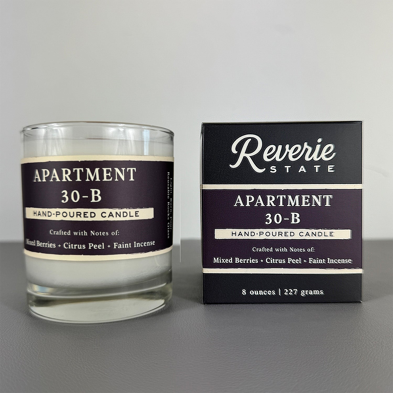 Hand-poured candle labeled 'Apartment 30-B' with its packaging on a gray background